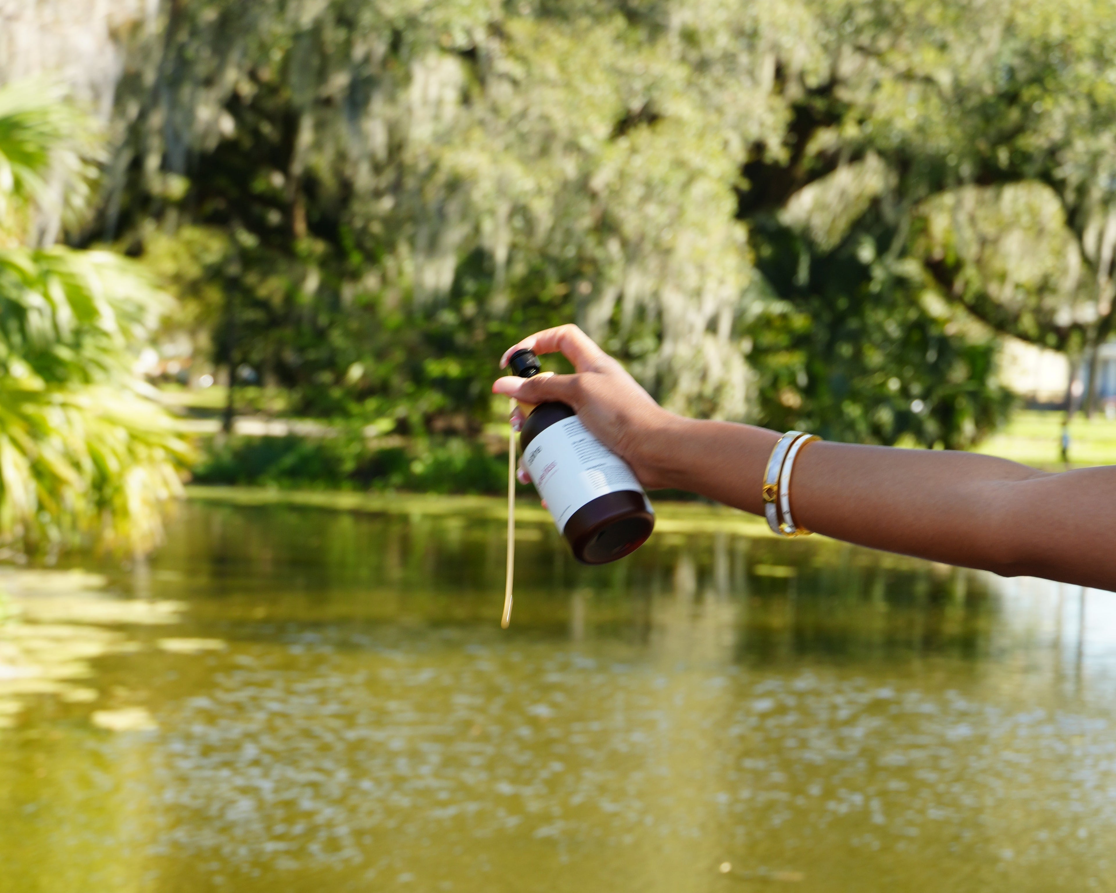 Person holding a bottle over a body of water with trees in the background